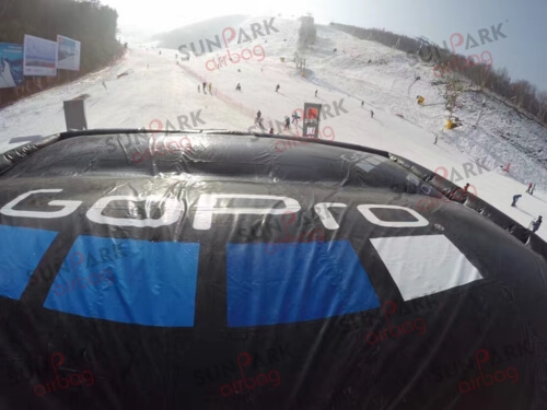 Looking down at a giant snowboarding airbag on a snowy ski slope, with skiers and snowboarders in the distance