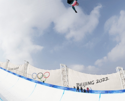 Valentino Guseli performing an inverted trick on his snowboard high above the halfpipe at the Beijing 2022 Winter Olympics