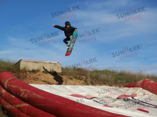 Young snowboarder launching off a jump towards a large red and white inflatable landing airbag